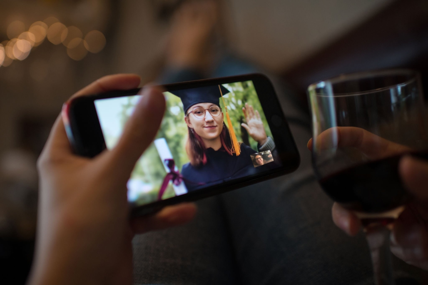 Teenage girl wearing graduation gown and cap greeting her relative or friend on video call